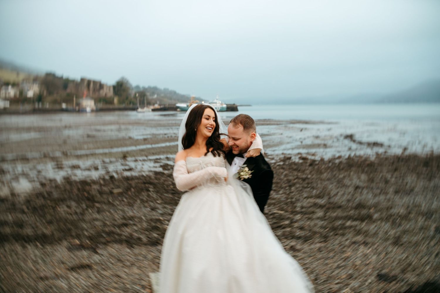 A couple shares an intimate moment on a rocky beach during overcast weather.