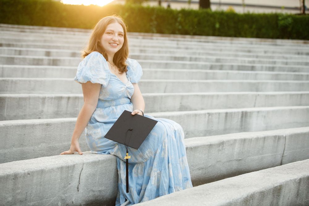 a woman poses with her graduation cap at the University of Arkansas Greek Theater.