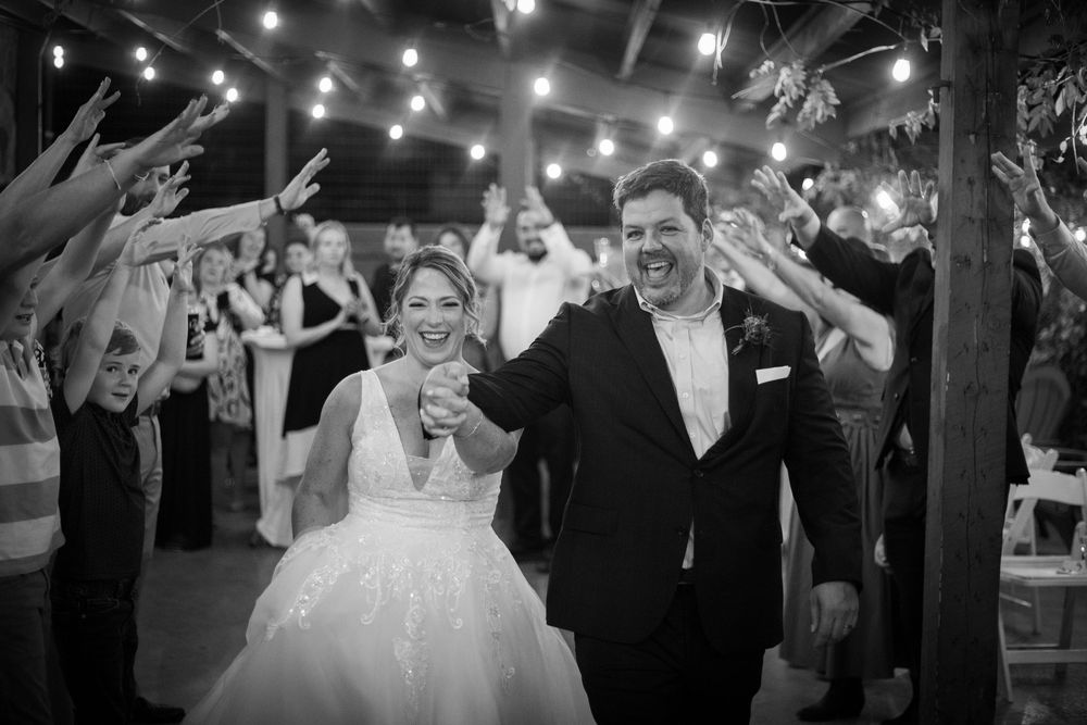 Wedding party dances and celebrates during evening reception under twinkling lights at indoor venue.