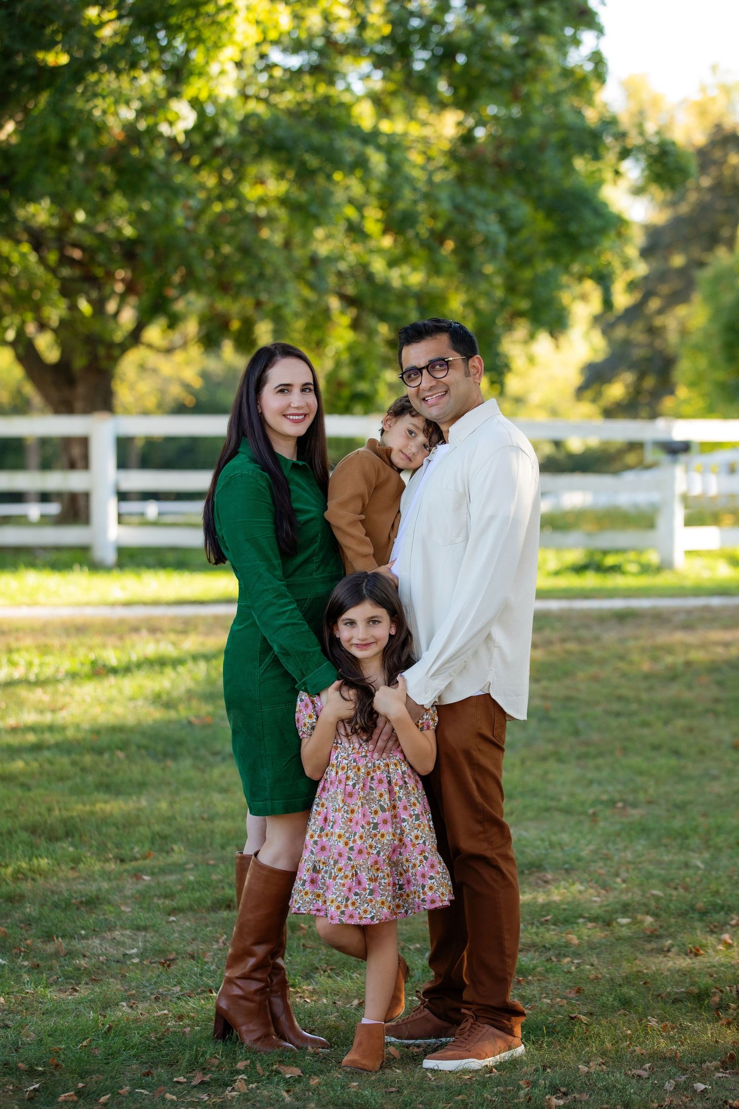 A family poses together outdoors in coordinating fall outfits near a white fence in a park setting.
