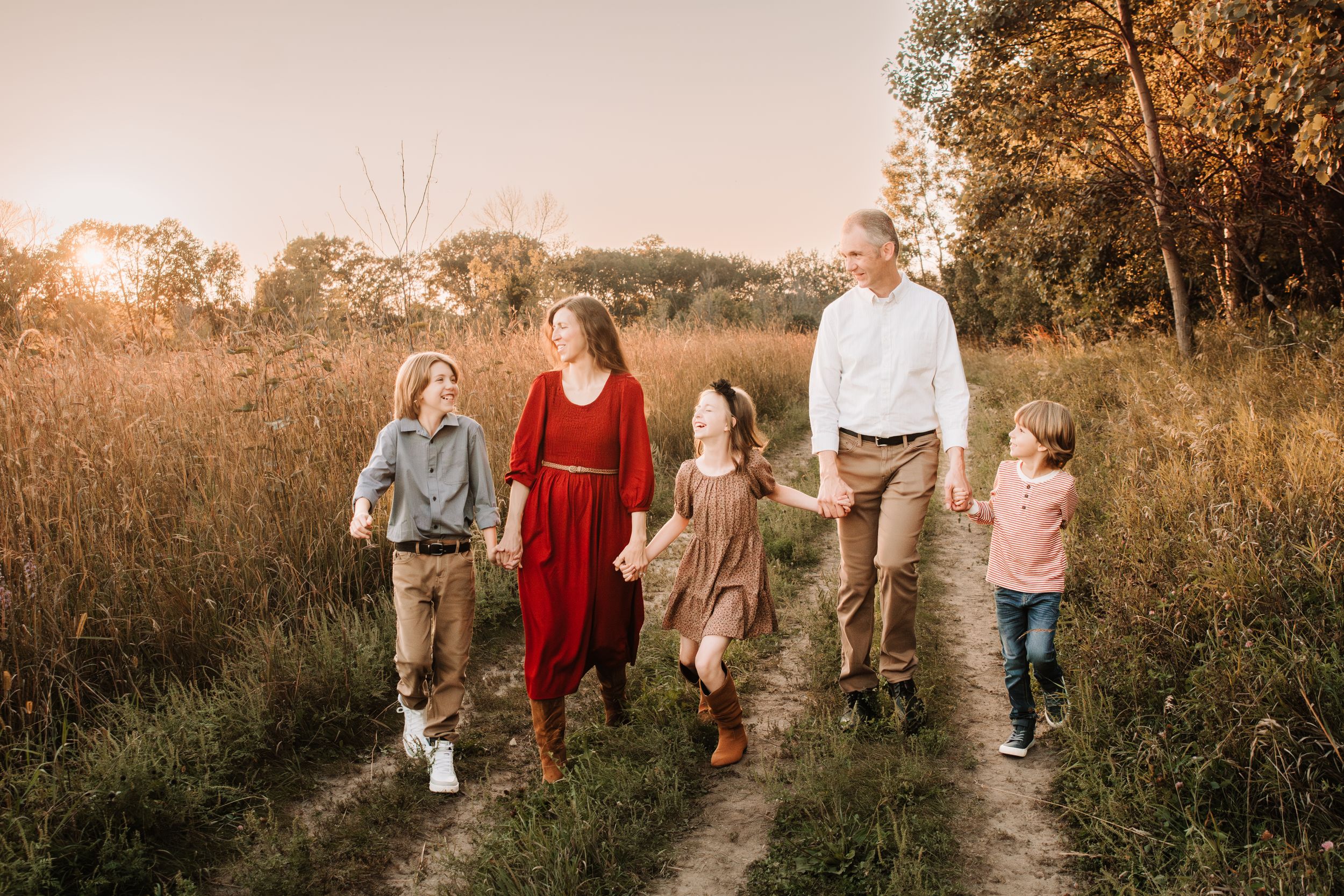 Family of five walking together on dirt path during golden hour sunset.