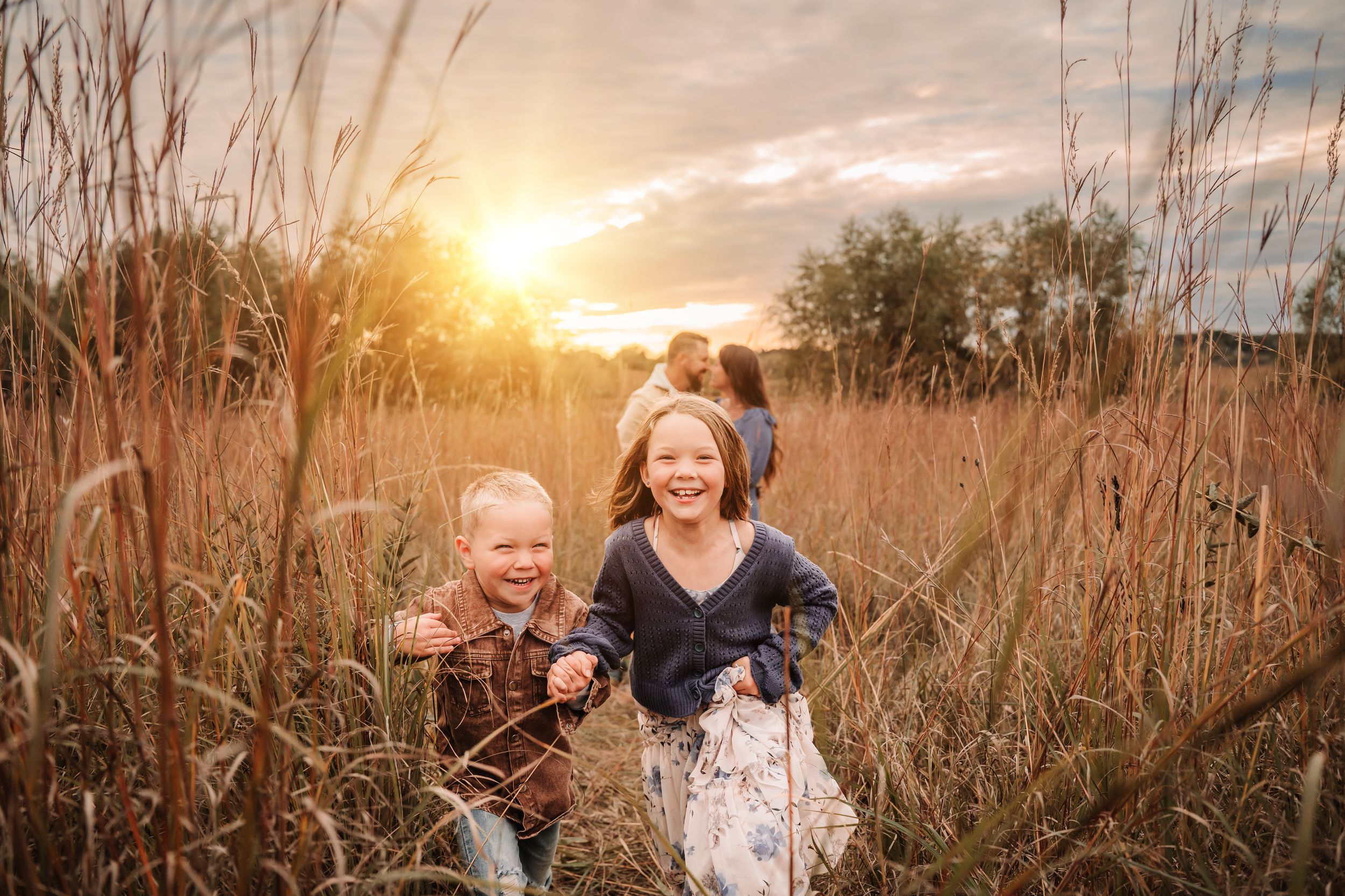 Family enjoying a golden sunset in a tall grass field during an outdoor photo session.