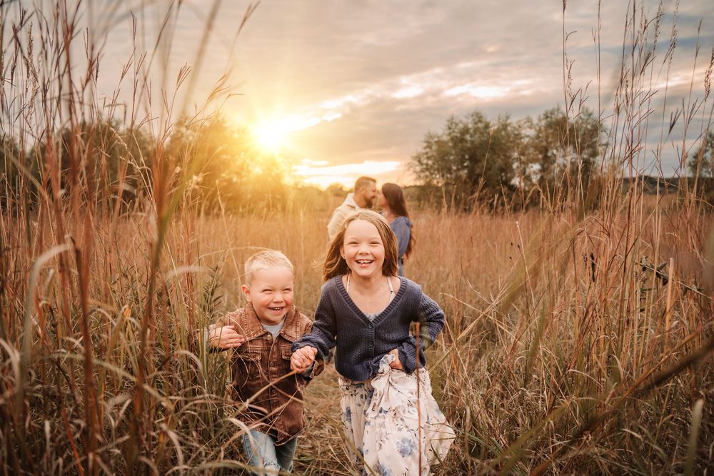 Family enjoying a golden sunset in a tall grass field during an outdoor photo session.