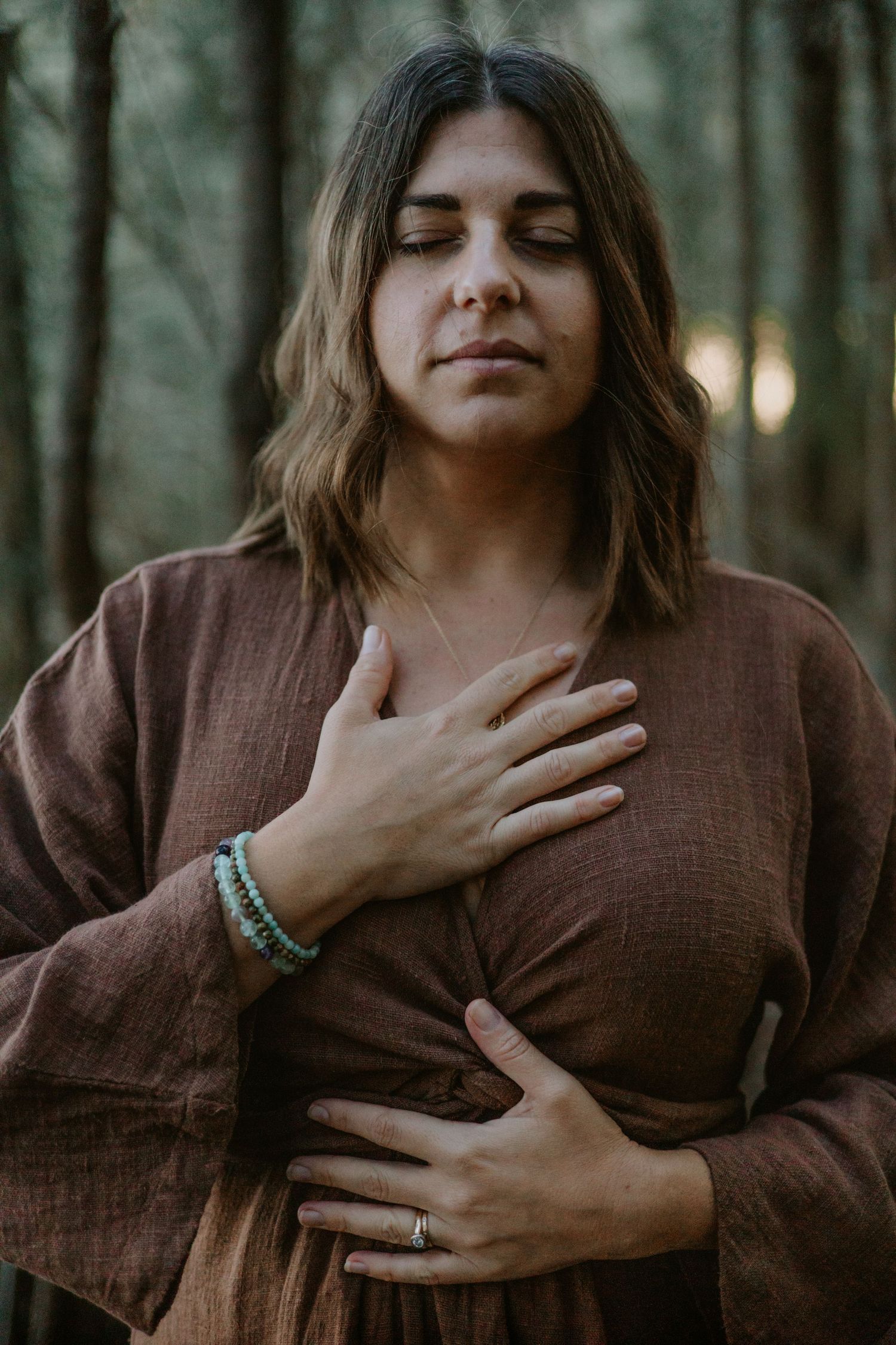 NSW South Coast branding photography – woman standing peacefully in the forest with hands on heart and stomach, captured in a natural, cand