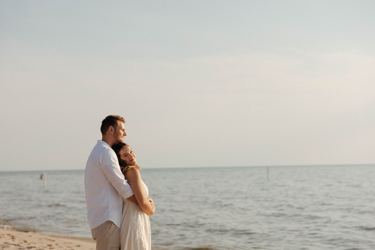 A couple shares romantic moments at Grand Haven during sunset, with multiple shots showing them embracing by the ocean.