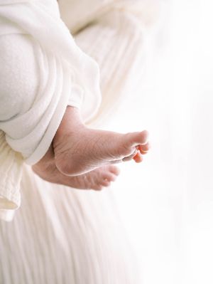 Tiny newborn baby feet wrapped in soft white blanket against light background.