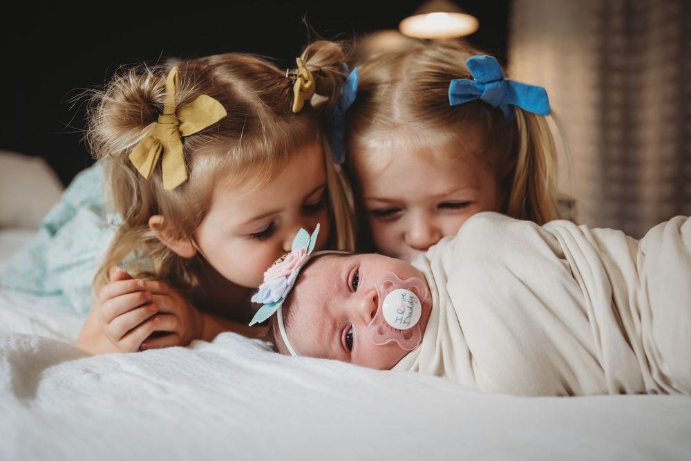 Three young children sharing tender moment together on white bedding.