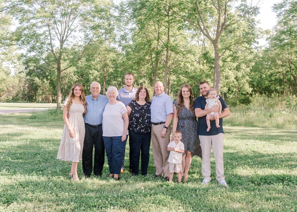 Large multigenerational family posing together outdoors in a lush green park setting on a sunny day.