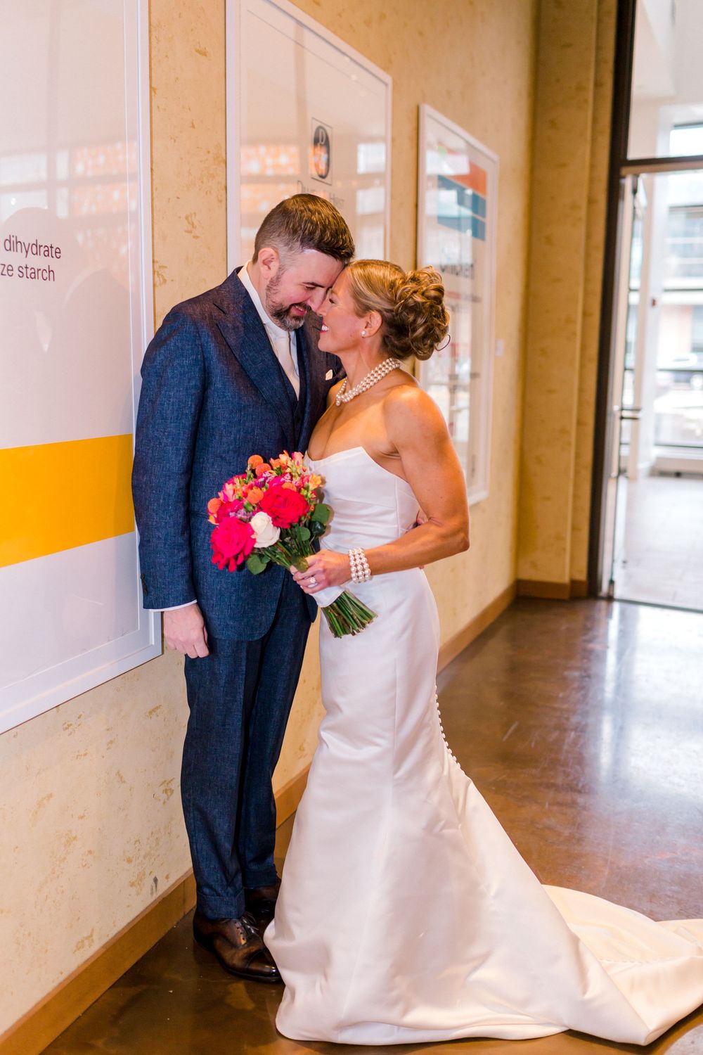Bride and groom share a romantic moment in a hallway, bride holding a vibrant pink bouquet.