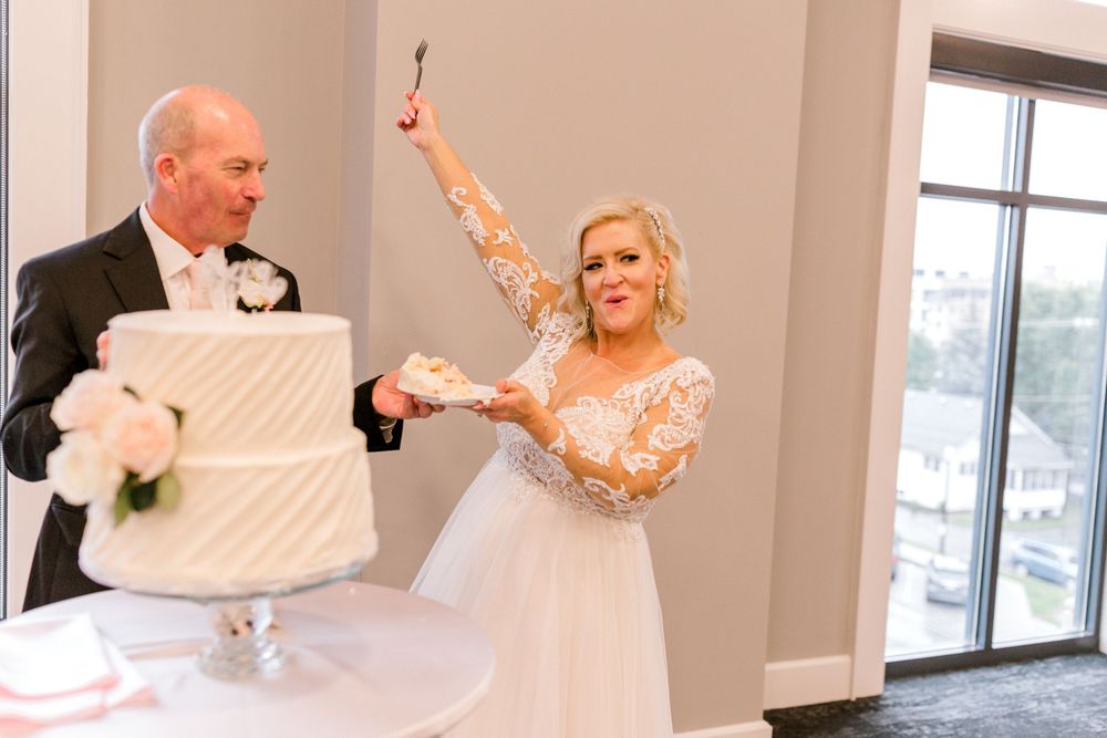 Bride and groom cutting their white wedding cake at reception, bride joyfully raising the knife.