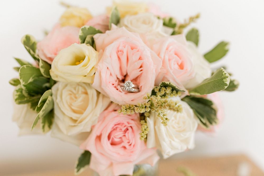 Elegant wedding bouquet of blush and cream roses with a sparkling diamond engagement ring.