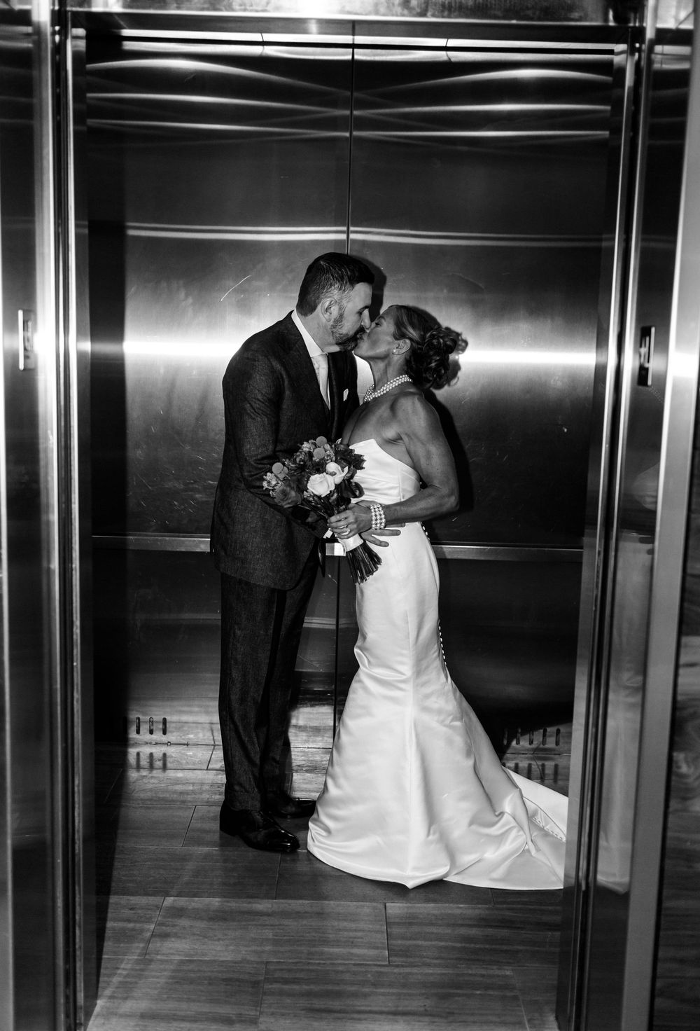 Black and white photo of bride and groom sharing a kiss in an elevator on their wedding day.