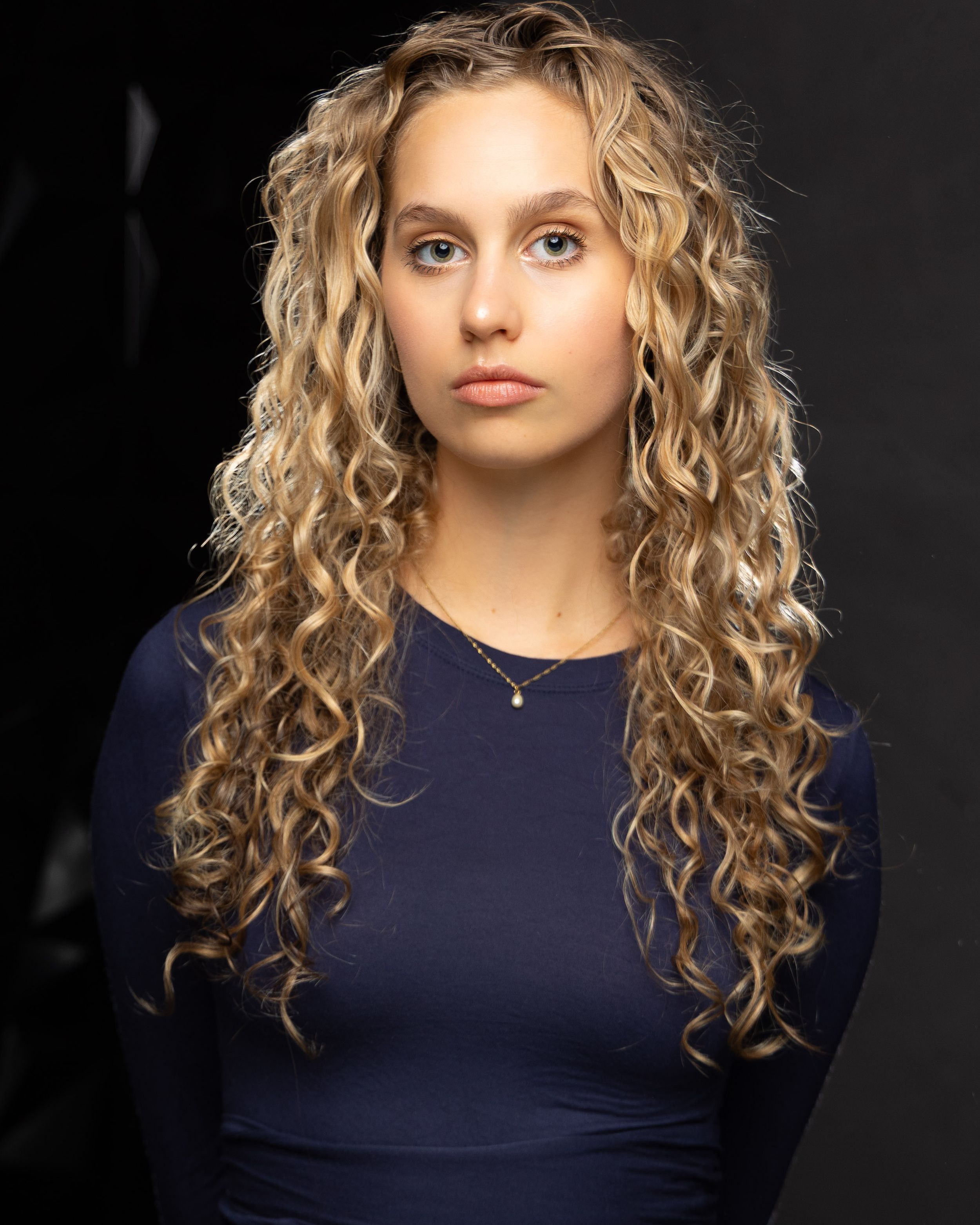 Studio portrait series featuring natural curly blonde hair and navy top against dark background.