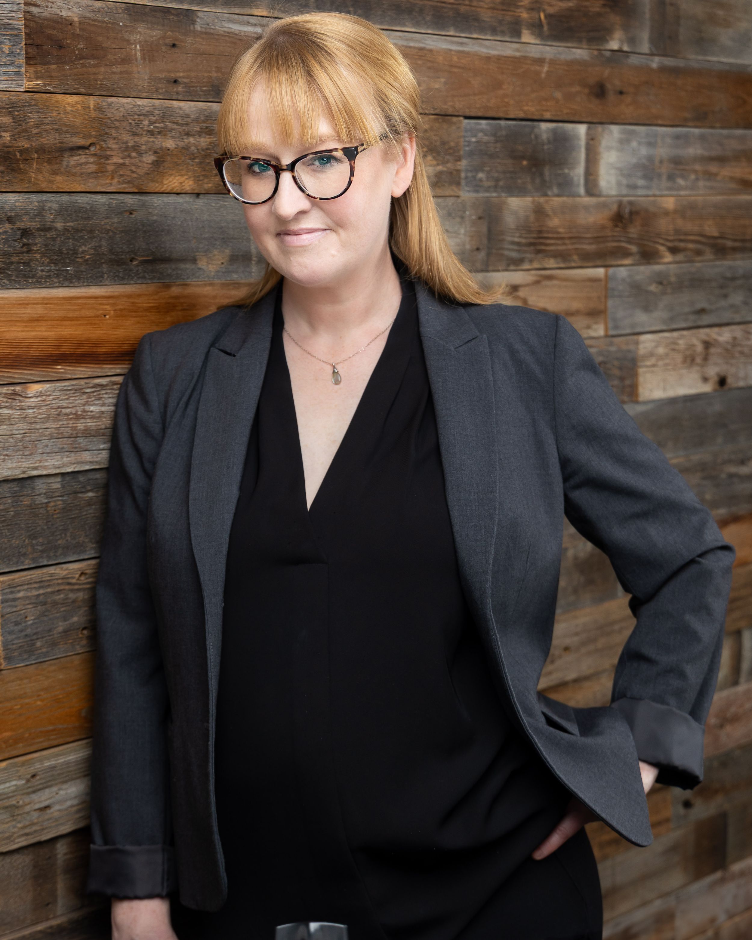 Professional headshots against rustic wood wall wearing black blazer and top.