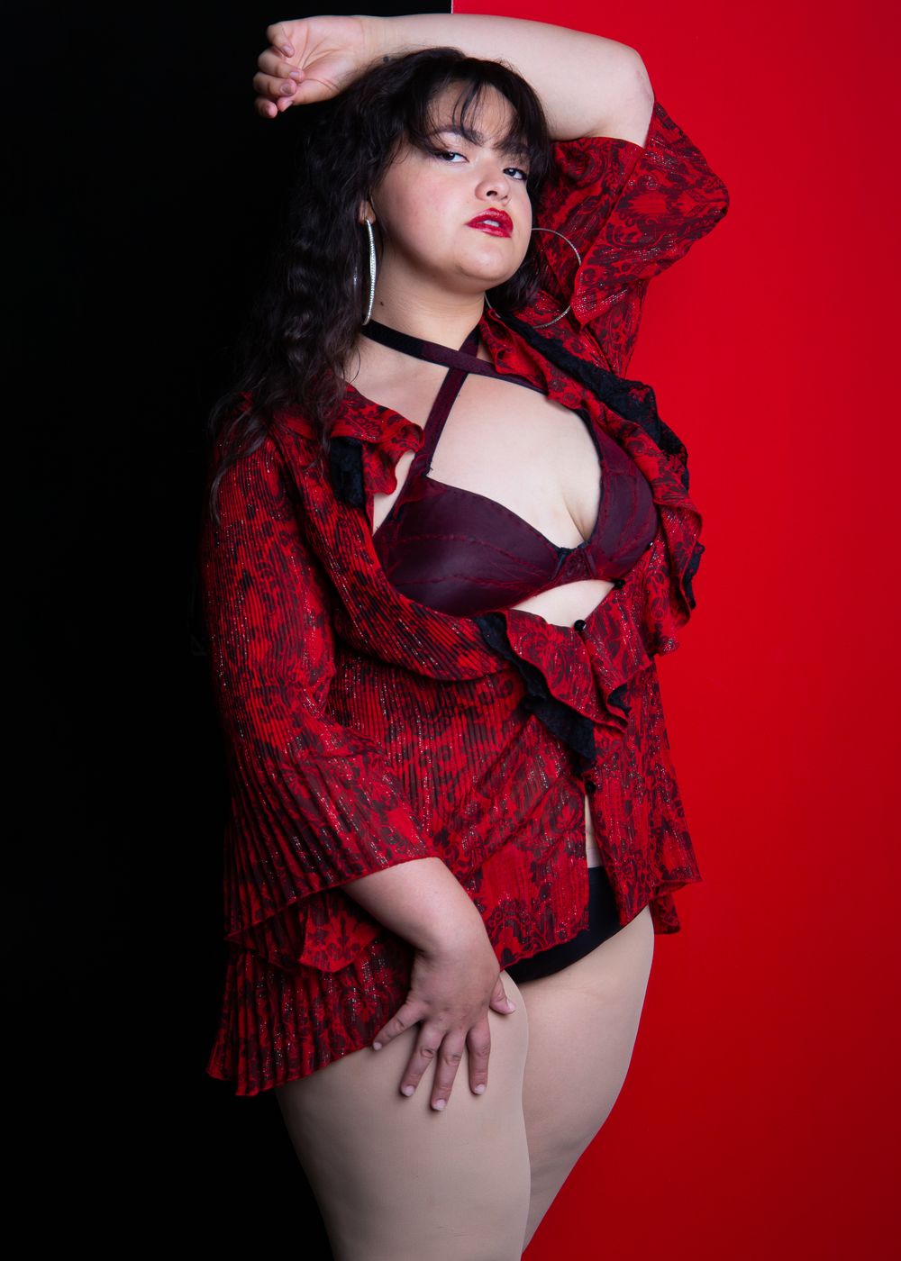 Burlesque portrait against red backdrop featuring black and red lace shawl styling.