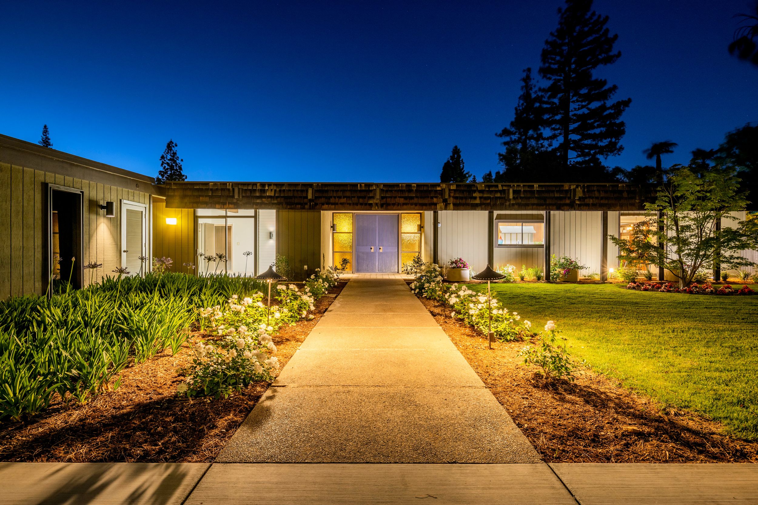 Illuminated driveway and garage entrance at night with warm lighting and landscaping creating an inviting atmosphere.