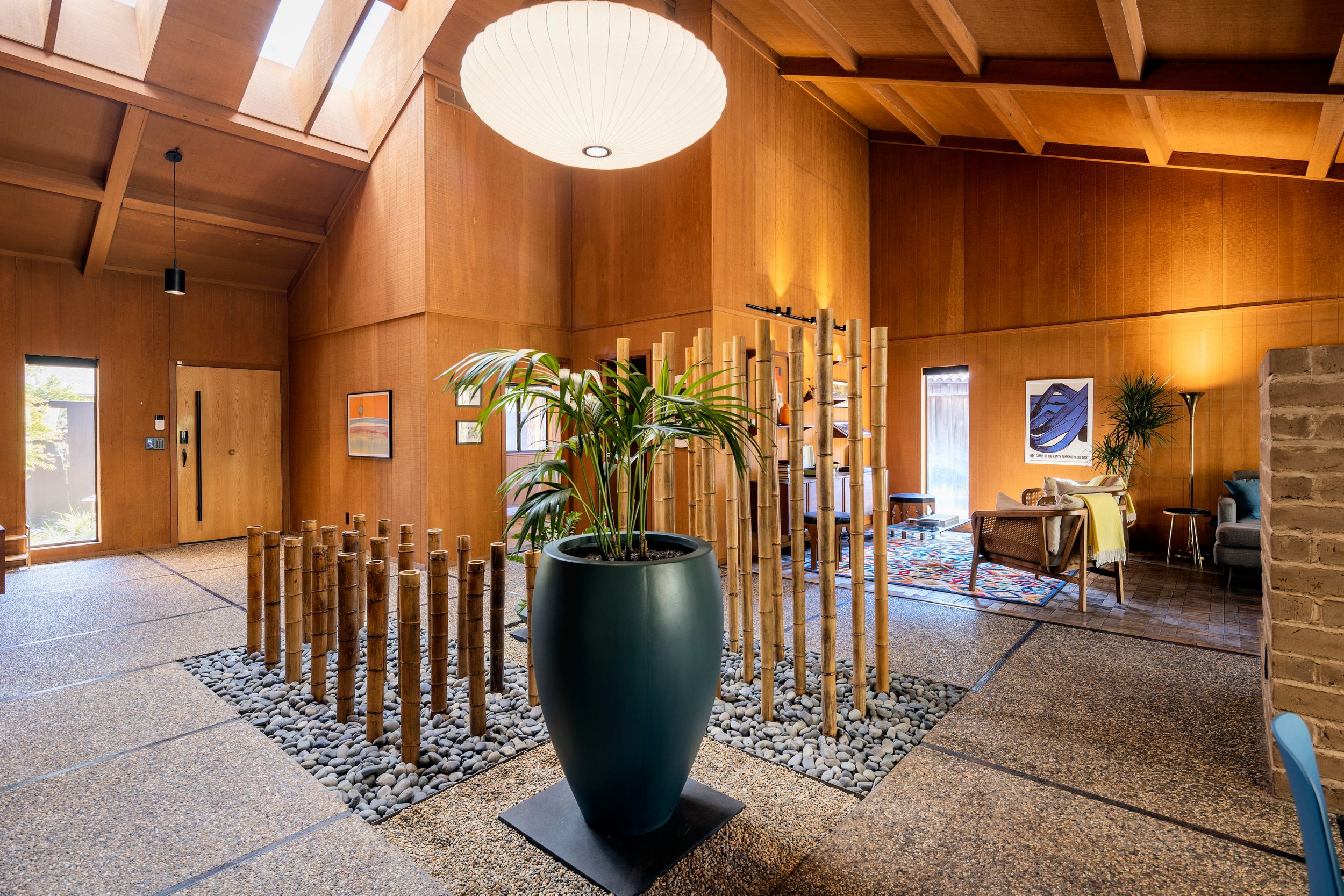 Modern lobby interior with wood paneling, bamboo decor, and a large black vase on a stone and pebble base.