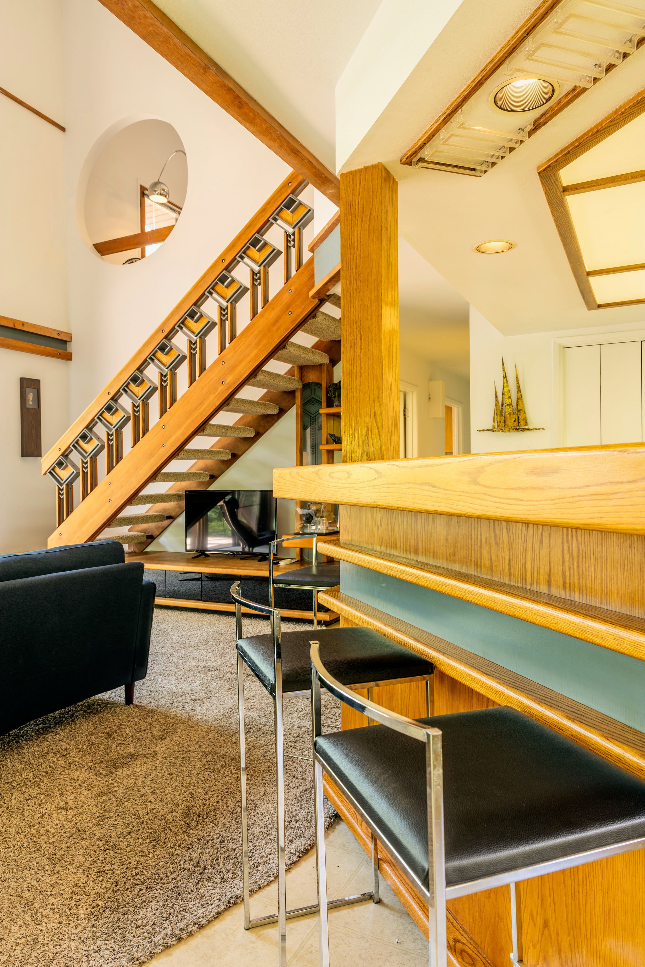 Modern mid-century interior with wooden staircase, black leather seating, and retro architectural details.