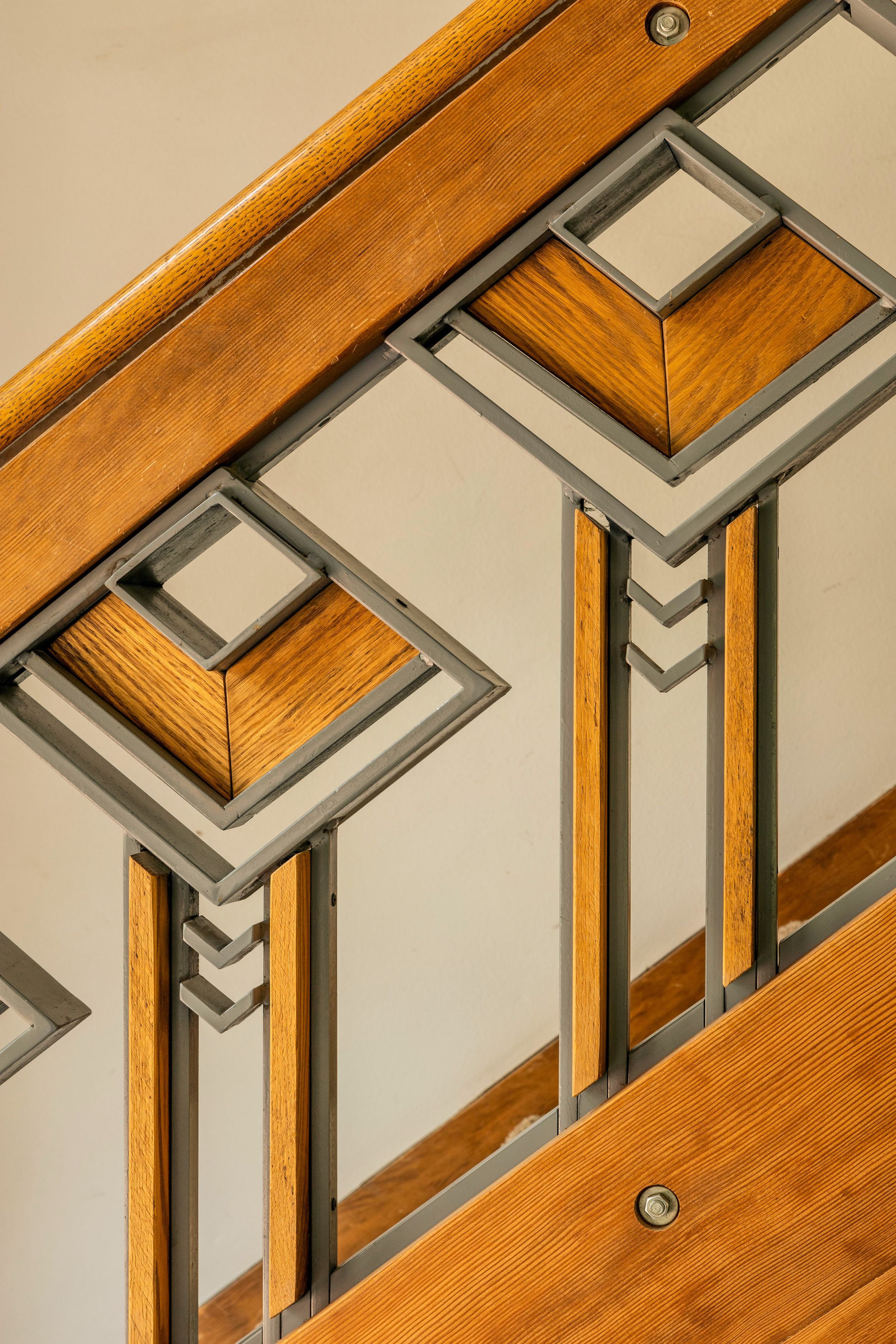 Close-up detail of Art Deco style wooden stair railing with geometric metal inlays and warm oak finish.