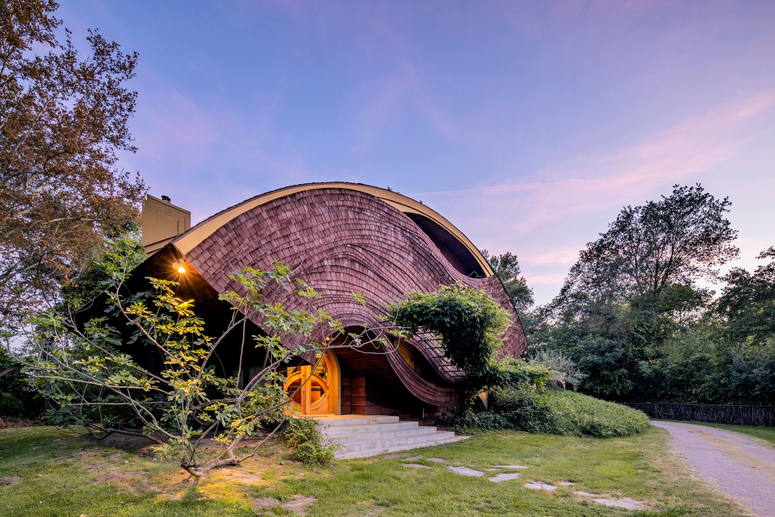 Hobbit-like curved building with wooden details and natural landscaping at sunset.