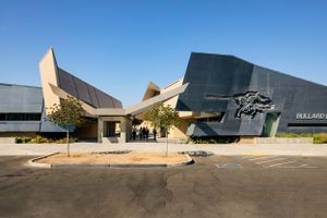 Modern museum building exterior with angular geometric architecture and metallic surfaces against blue sky.