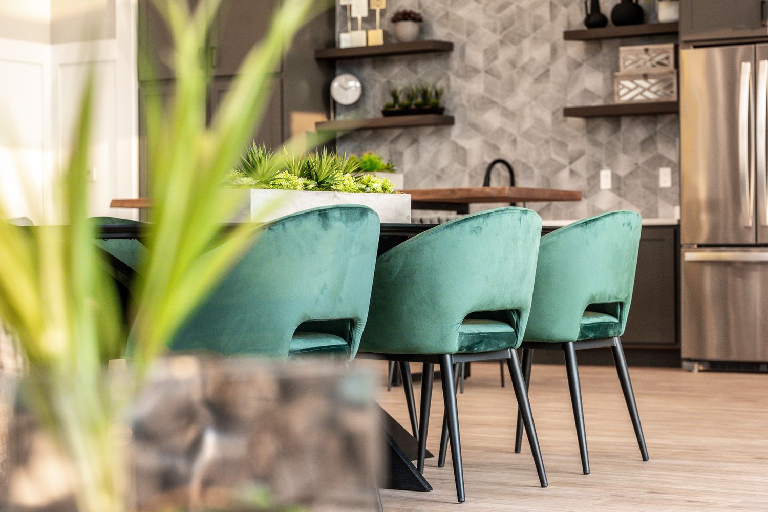 Multifamily clubhouse kitchen at The Levi Apartments in St. Petersburg, FL, featuring green chairs, geometric backsplash, and modern design.