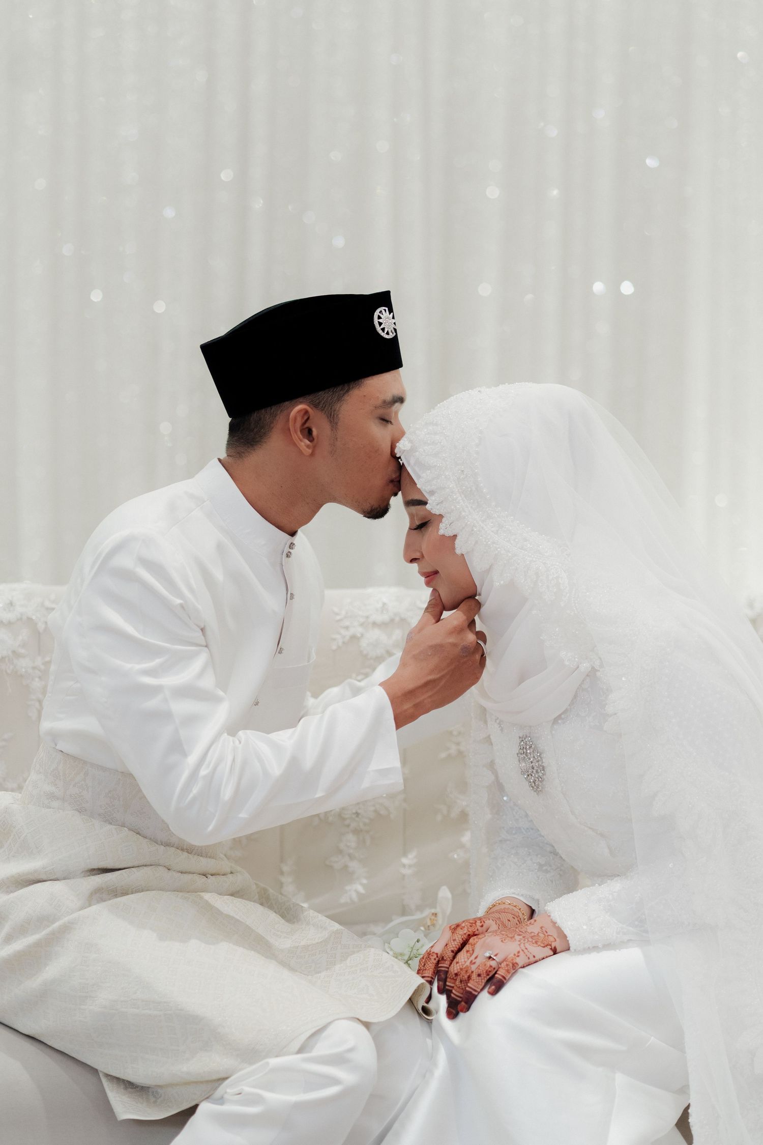 Wedding details showing henna-decorated hands with floral bouquet on white lace dress.