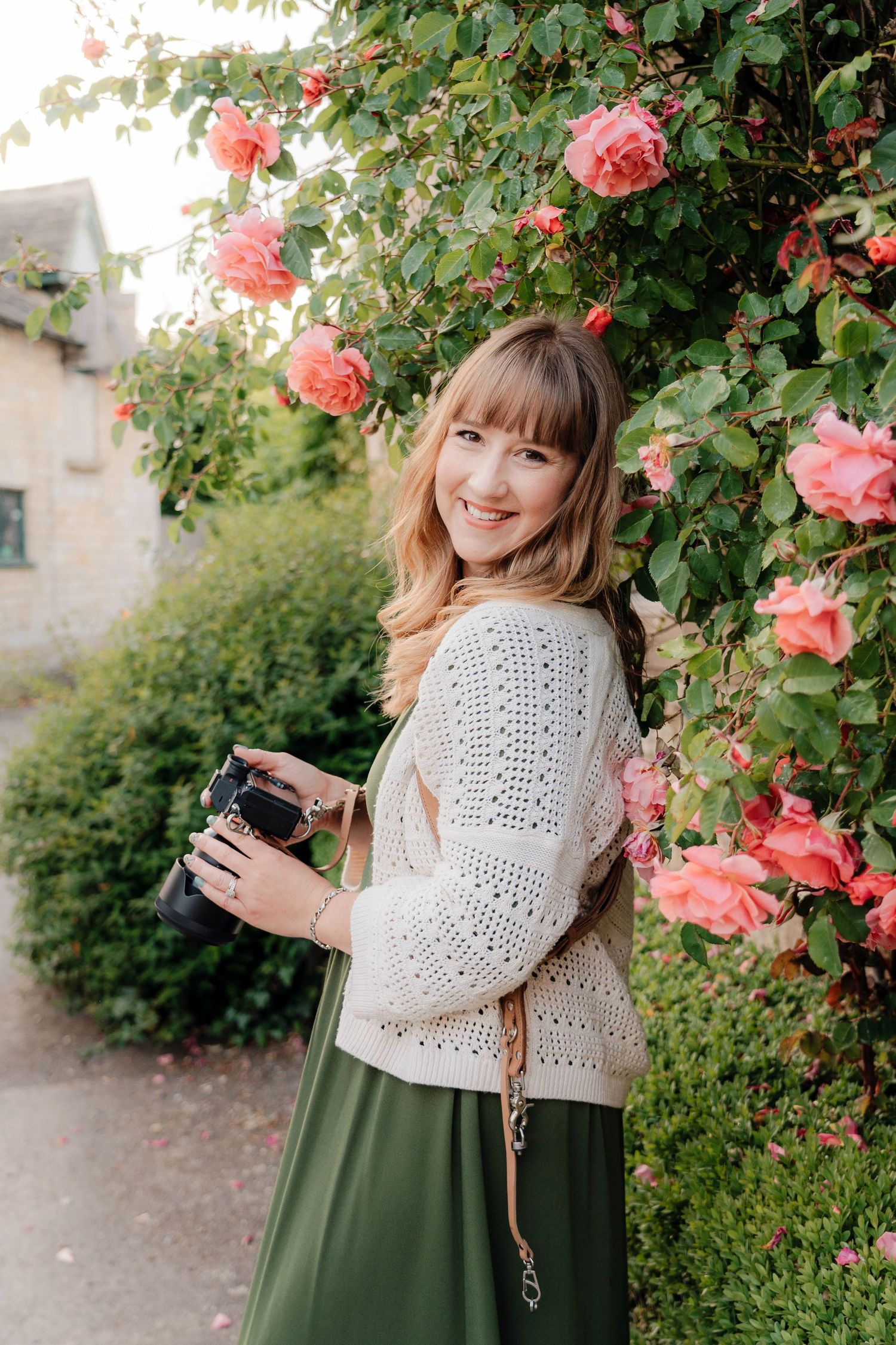 Photo of lisa from pausing time photography holding camera amongst rose bush in Lower Slaughter Cheltenham