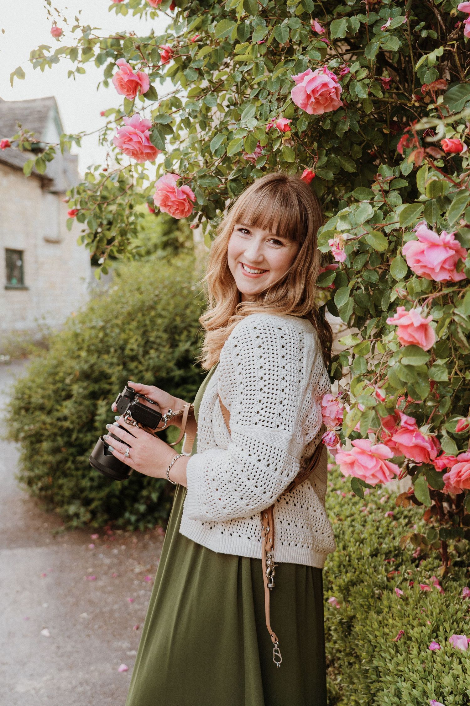 Photo of lisa from pausing time photography holding camera amongst rose bush in Lower Slaughter Cheltenham