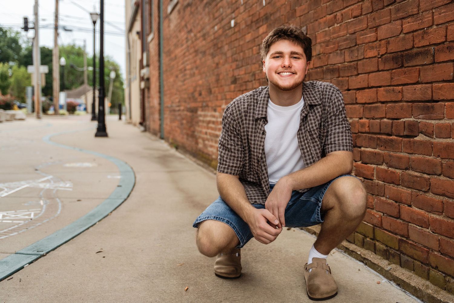 Person in casual attire sits against rustic brick wall in urban setting during outdoor portrait session.