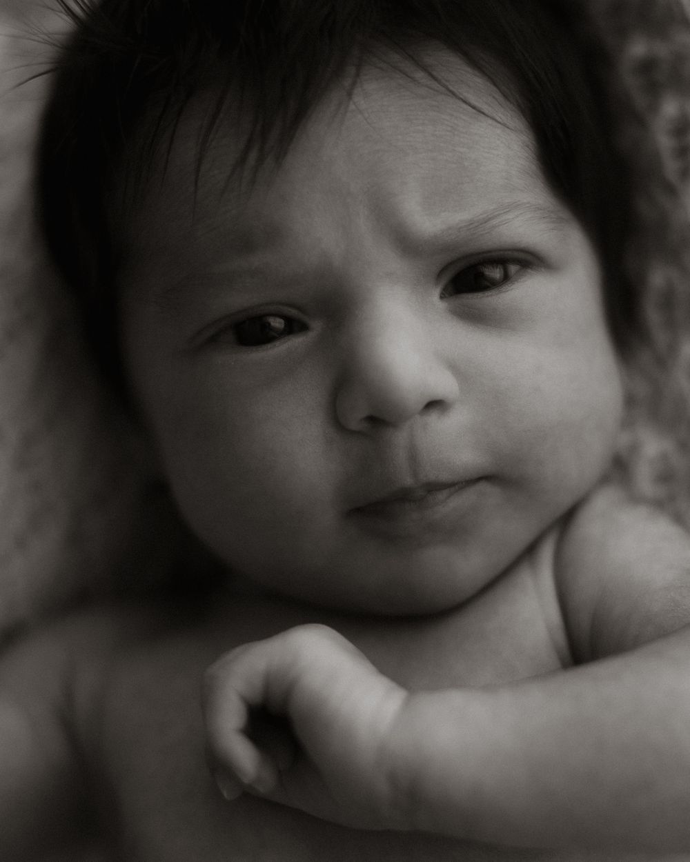 svart hvitt nærbilde av baby med mye sort hår med uttrykksfullt ansikt.