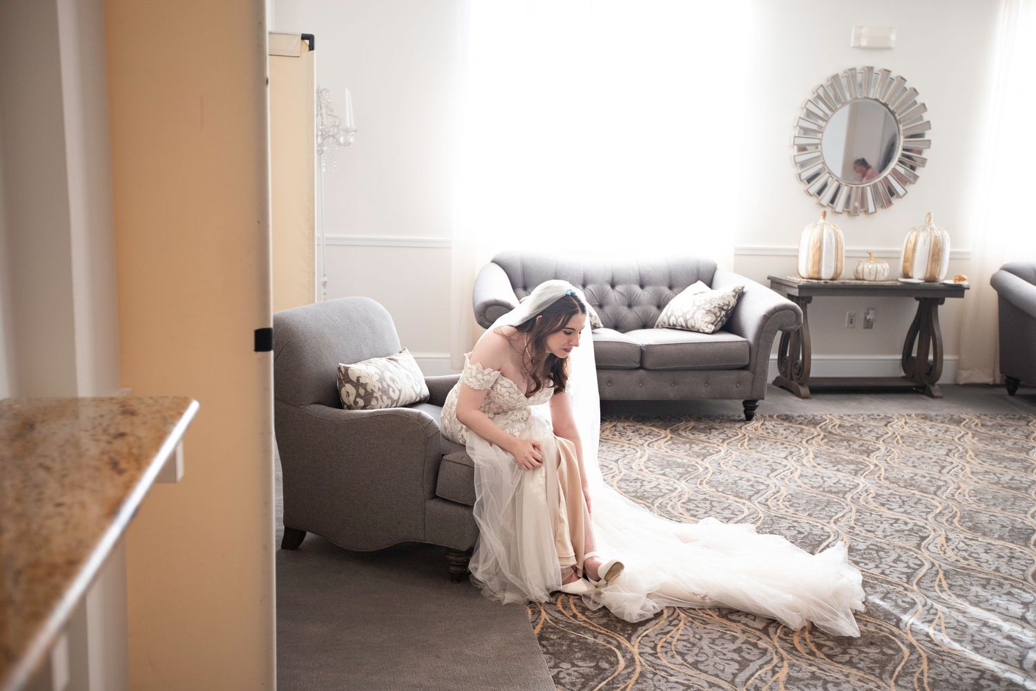 Bride in full lace wedding gown sitting quietly on a gray armchair in an elegant bridal suite.