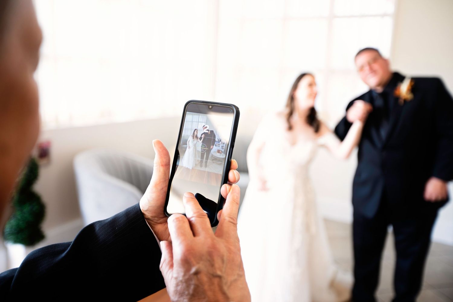 Wedding photographer capturing bride and groom portrait on smartphone at bright indoor venue.