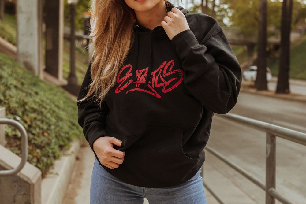 Person wearing black hoodie with red text design poses against outdoor railing.