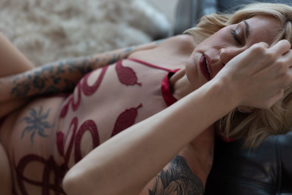 A relaxed figure wearing floral print lounges on a couch, with visible tattoo art and soft lighting.