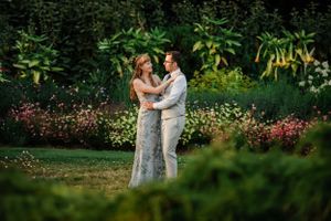 Couple embraces in lush garden setting surrounded by flowers and greenery.