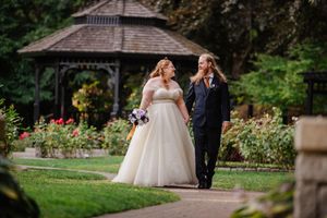 A romantic scene between a couple in formal wedding attire in a lush garden with blooming flowers.