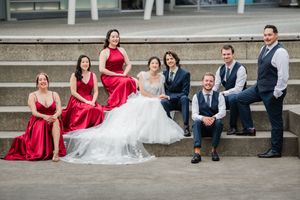 Wedding party members sit casually on stone steps wearing red dresses and navy suits for a relaxed group photo.