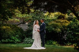 A couple in wedding attire stands together in a lush garden setting during their celebration.