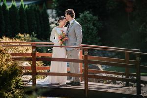 Couple holds hands while walking on wooden bridge railing in outdoor park setting during sunset.