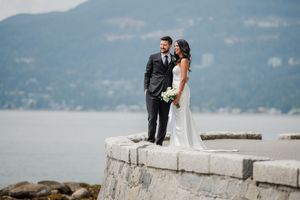 Wedding couple posing on a jetty by a lake with mountains in the background on a cloudy day.