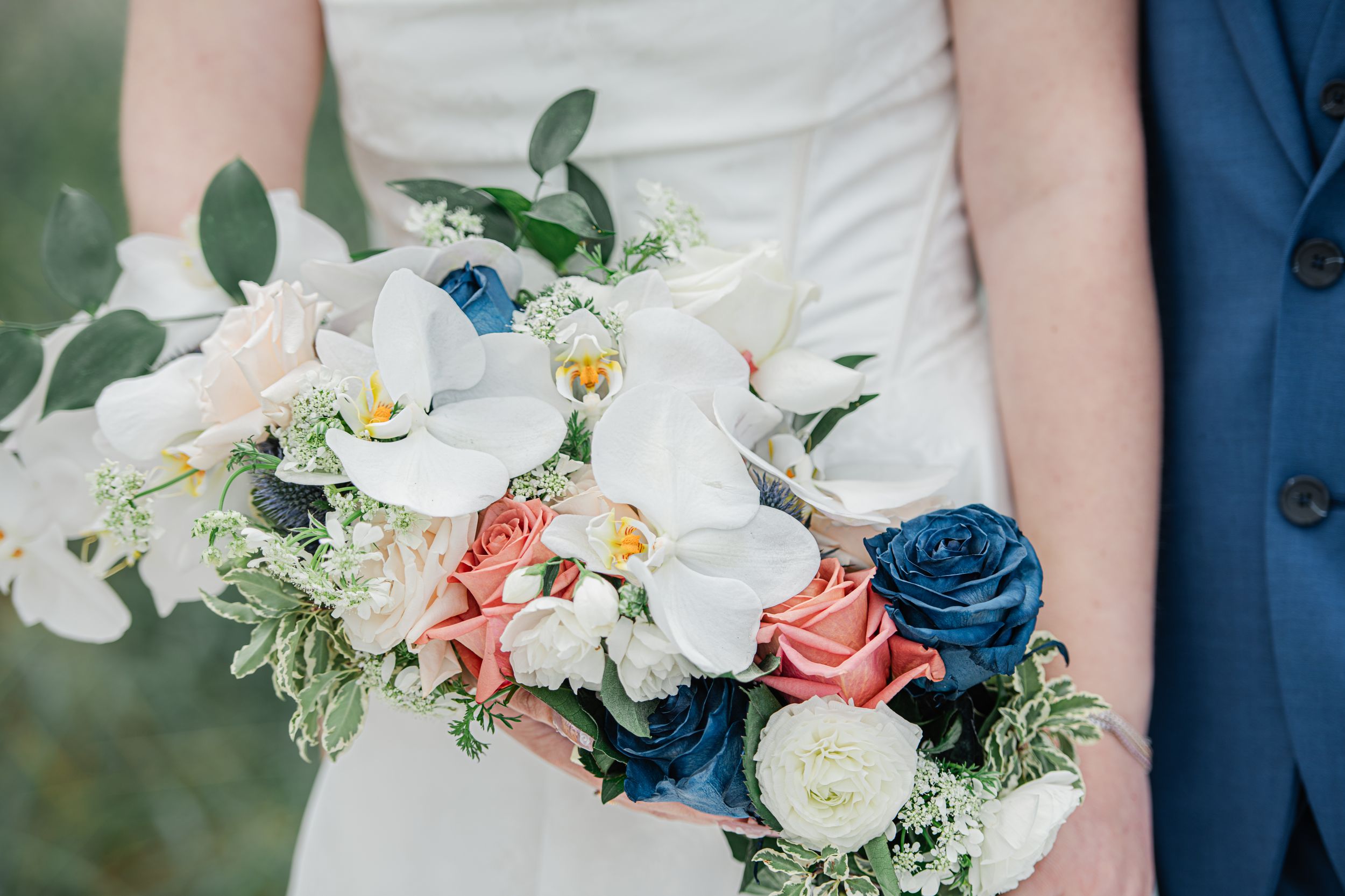 Bride holding a lush wedding bouquet with white orchids, pink roses, blue ranunculus, and greenery.