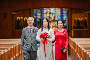 Wedding party members in grey suits and red attire pose together in a traditional church setting.