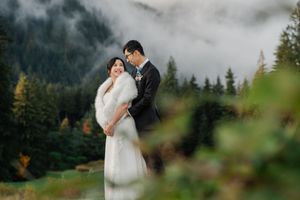 A couple in wedding attire embraces in a misty evergreen forest setting during their outdoor ceremony.