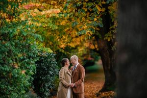 A couple embraces under vibrant autumn trees with golden leaves during an outdoor photoshoot.