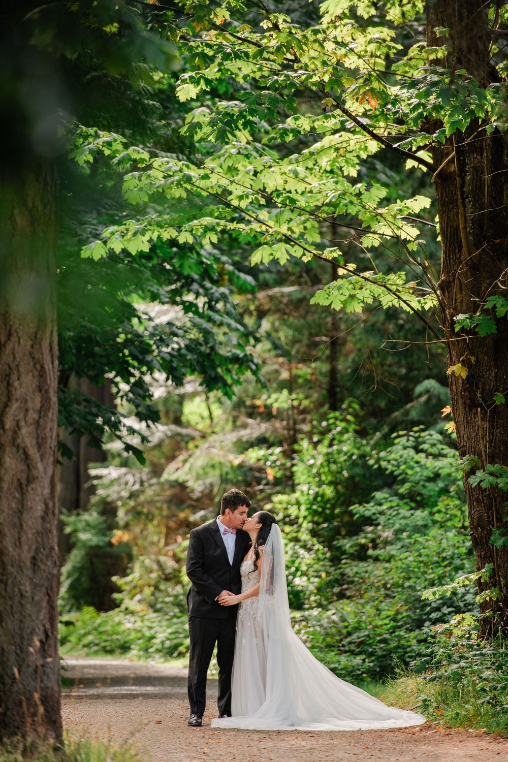 Bride and groom sharing a romantic moment on a forest path surrounded by lush green trees on their wedding day.
