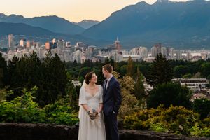 A couple stands on a viewpoint overlooking Vancouver's skyline with mountains in the background at sunset.