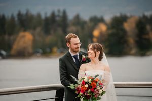 A couple in wedding attire shares a romantic moment by a serene lake during their outdoor ceremony.