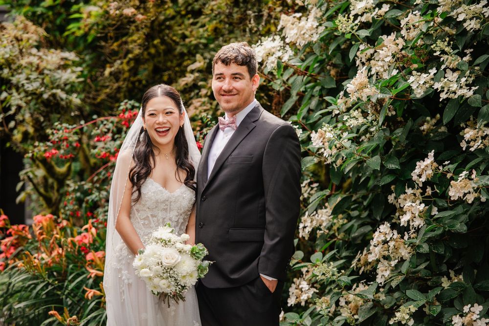 Bride and groom smiling together in a lush garden, bride holding white bouquet in elegant strapless wedding gown.