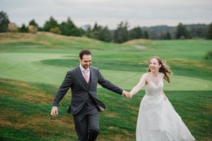 A couple walks hand in hand on rolling green golf course hills during their wedding celebration.